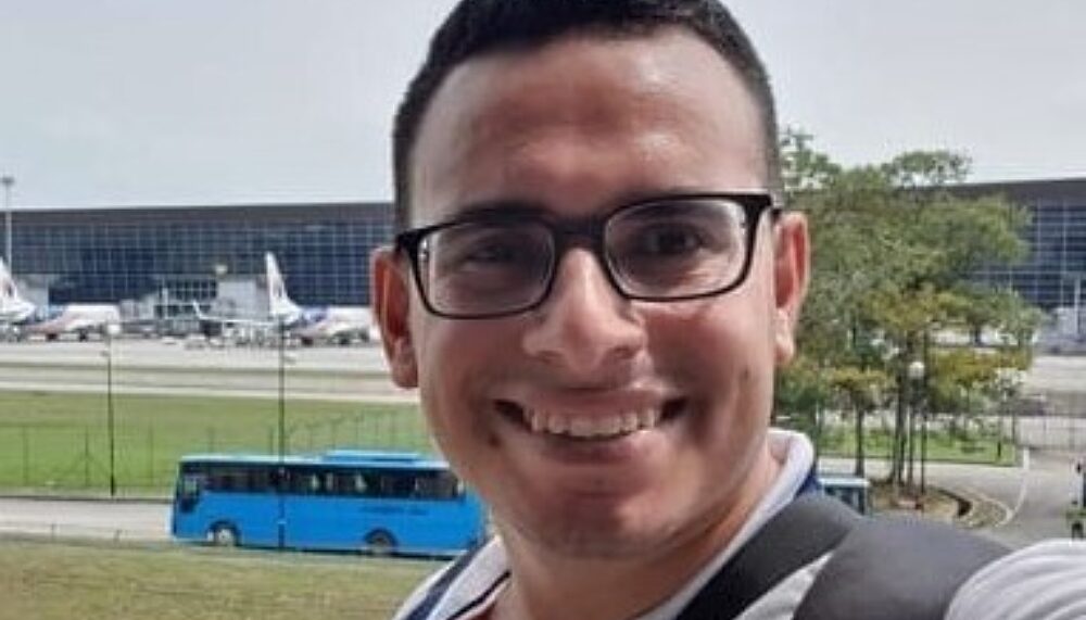 Photo of Mahmoud Alnaouq. Mahmoud is standing in front of an airport and he is smiling into the camera. Mahmoud was killed in the shelling of Gaza, alongside his family, at the end of October 2023.
