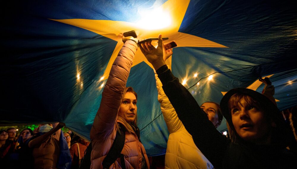 Demonstrators shine the lights of their mobile phones as they stand under a large European Union flag, during a pro-EU rally ahead of the second round of the presidential election redo in Bucharest, Romania, Friday, May 9, 2025.